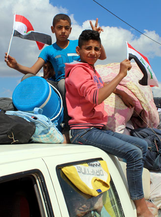 Displaced Iraqi boys sit on top of a vehicle waving their national flag in a queue for security checks, as some 250 families return to their hometowns in the area of Husaybah and Juwaybah in Iraq’s Anbar province on Tuesday (AFP photo)