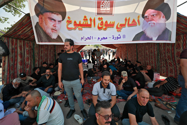Supporters of Iraqi Shiite cleric Moqtada Sadr sit in a tent beneath a banner depicting Sadr (left) and his late father Grand Ayatollah Mohammed Sadeq Sadr, outside the headquarters of the Supreme Judicial Council, Iraq's highest judicial body, in the capital Baghdad, on Tuesday (AFP photo)