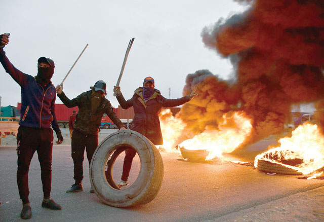 Iraqi protesters pose in front of burning tyres, blocking an international highway in the southern city of Nasiriyah, on Tuesday, amid ongoing anti-government demonstrations (AFP photo)