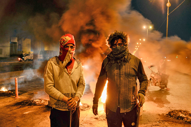 Masked anti-government protesters stand before flaming tyres at a make-shift roadblock in the central Iraqi holy shrine city of Najaf, on Saturday (AFP photo)