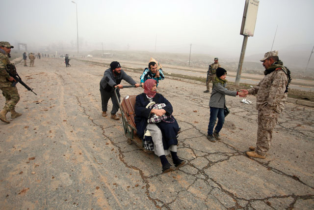 Displaced people, who left their homes due to war, travel past Iraqi soldiers during a battle with Daesh militants in the Arabi neighbourhood, north of Mosul, Iraq,  on Monday (Reuters photo)