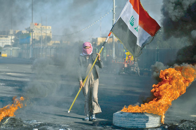An anti-government protester waves a national flag as he stands before flaming tyres at a make-shift roadblock during a demonstration in the central Shiite holy shrine city of Najaf on Sunday (AFP photo)