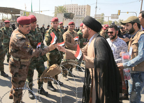 Shiite cleric Ibrahim Al Jabiri, director of Muqtada Al Sadr’s offices in Baghdad and northern provinces, hands an Iraqi flag to security forces, as a gesture of cooperation between protesters and troops, during a sit-in by Sadr supporters outside the heavily secured Green Zone in Baghdad, on Saturday (AP photo)