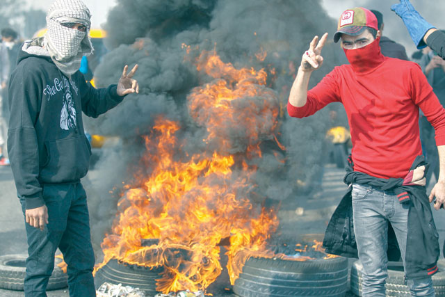 Iraqi protesters flash the victory sign as they burn tyres during an anti-government demonstration on Mohammad Al Qasim highway in east Baghdad on Tuesday (AFP photo)