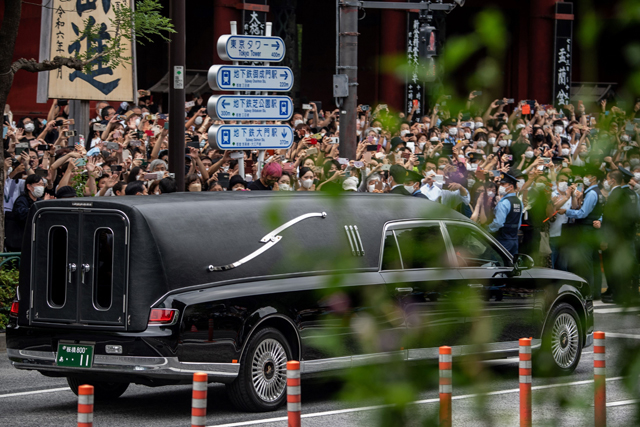 People watch the hearse transporting the body of the late former Japanese prime minister Shinzo Abe as it leaves Zojoji Temple in Tokyo on Tuesday (AFP photo)