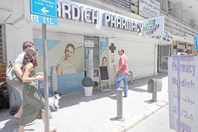 People walk in front of the shuttered door of a pharmacy in the Lebanese capital Beirut, during a nationwide strike of pharmacies to protest against a severe shortage of medicine, on Friday (AFP photo)