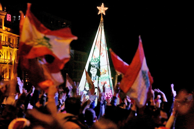 Lebanese anti-corruption protesters wave the national flag in front of a Christmas tree erected in Martyr's Square in downtown Beirut on Sunday (AFP photo)
