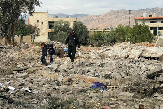 A man and two children walk above debris at the site of an overnight Israeli airstrike in the eastern Lebanese village of Al Qasr, on Monday (AFP photo)