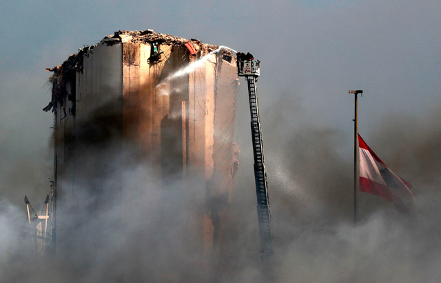 Lebanese firefighters stand on a ladder amid billowing smoke as they extinguish the remaining flames at the Beirut port on Friday, a day after a huge fire erupted in harbour warehouses (AFP photo)