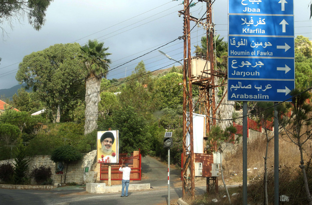 A Lebanese man takes photos of a street billboard bearing a portrait of the head of the Shiite movement Hizbollah Sayyed Hassan Nasrallah at the entrance of in Ain Qana, where an explosion rocked a Hizbollah site earlier in the southern village, on Tuesday (AFP photo)