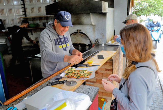Abu Shadi (centre), 54, sprinkles a freshly baked garnished flatbread with lemon juice as he serves a customer in his bakery in the Ras Beirut area of the Lebanese capital Beirut, on Saturday (AFP photo)