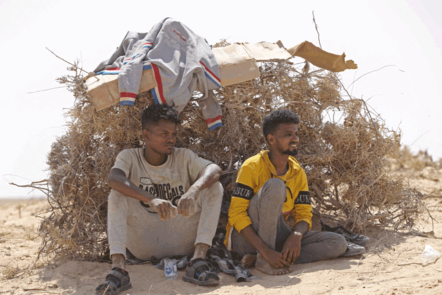 Migrants from sub-Saharan African countries who claim to have been abandoned in the desert by Tunisian authorities, shield themselves from the scorching summer heat in an uninhabited area near the border town of Al Assah on Sunday (AFP photo)