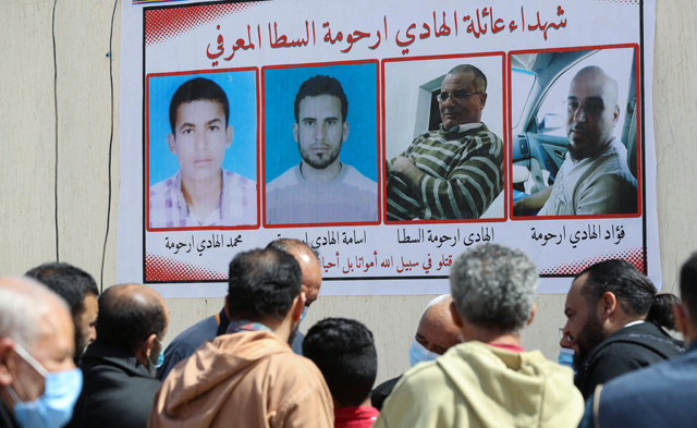 Libyans gather by a wall poster depicting victims from one family during a funeral procession for 12 bodies that were identified from mass graves found in Tarhuna town, 80Km southeast of the capital, on March 26 (AFP photo)
