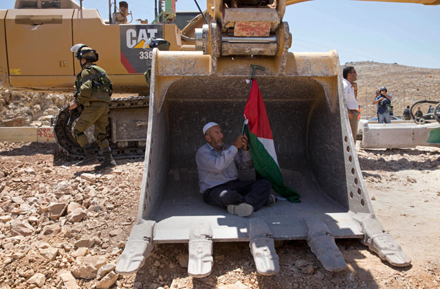 A Palestinian man tries to stop work by an Israeli bulldozer during a protest outside the village of Deir Qaddis, near the West Bank city of Ramallah, Wednesday (AP photo)