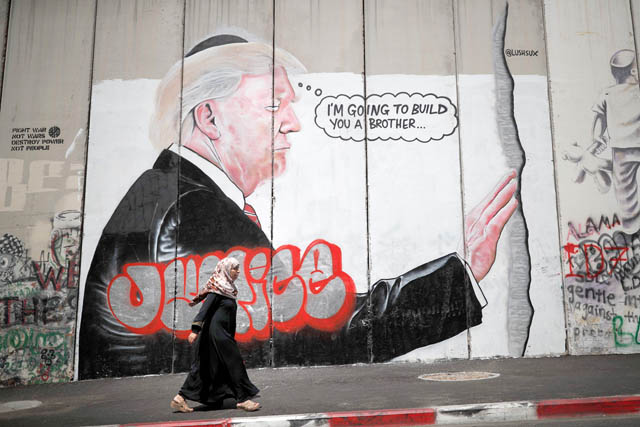 A woman walks past graffiti depicting US President Donald Trump on the controversial Israeli separation barrier separating the West Bank town of Bethlehem from Jerusalem on Friday (AFP photo)