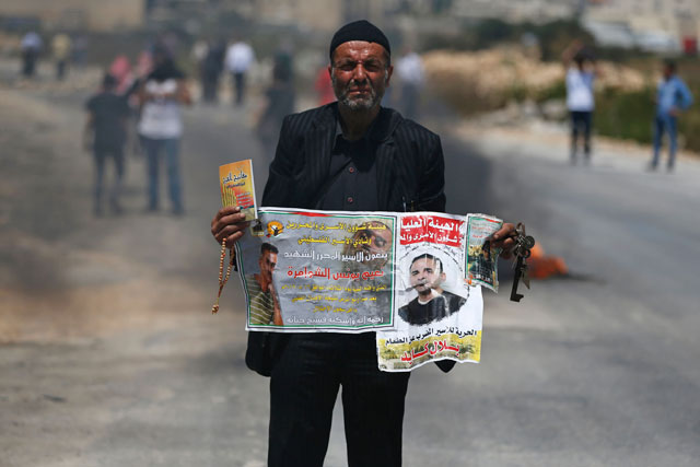 A man holds posters against administrative detention and in support of Palestinian prisoners held in Israeli jails during a protest in front of the Israeli-run Ofer prison in the West Bank village of Betunia, on Thursday (AFP photo)