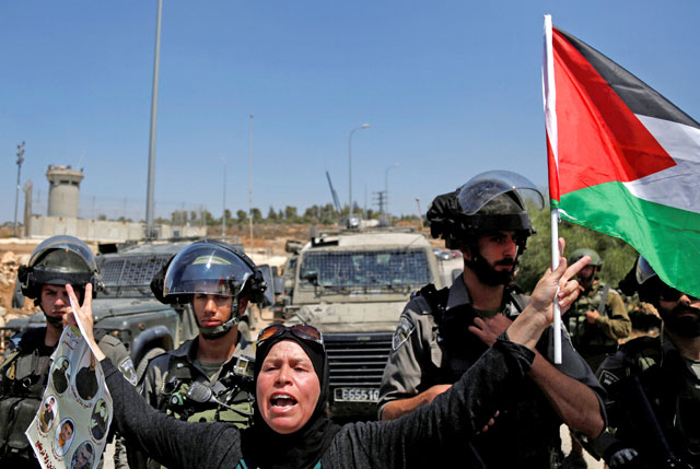 A woman gestures as she holds a Palestinian flag in front of Israeli soldiers during a protest in solidarity with Palestinian prisoners held in Israeli jails in the West Bank village of Nabi Saleh, near Ramallah, on Friday (Reuters photo)