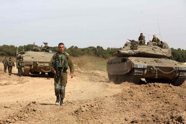 Israeli forces stand guard next to a tank and an APC (armoured personal carrier) along the border between Israel and the Gaza Strip near the southern Israeli Kibbutz of Nahal Oz on Wednesday (AFP photo)