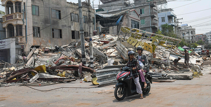 People ride a motorbike past damaged buildings in Mandalay on Sunday (AFP photo)