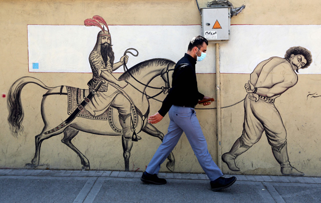 A man, wearing a protective mask due to the COVID-19 coronavirus pandemic, walks past a graffiti depicting the legendary Persian hero Rustam  riding his horse behind a bound prisoner in Iran's capital Tehran, on Sunday (AFP photo)