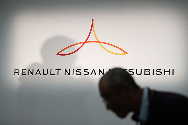 In this file photo taken on March 12, 2019, a member of the media walks in front of a logo showing Renault, Nissan and Mitsubishi ahead of a press conference at the Nissan headquarters, in Yokohama, Kanagawa prefecture (AFP photo)
