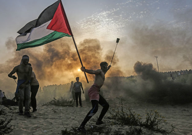 A Palestinian protester holds a national flag as he throws a stone towards Israeli occupation forces during a demonstration on the beach near the maritime border with Israel, in the northern Gaza Strip, on Monday (AFP photo)