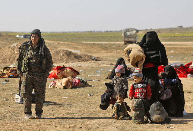 A member of the Kurdish women's protection units, part of the Syrian Democratic Forces (SDF), walks alongside women waiting with children fleeing the battered Daesh-held holdout of Baghouz in the eastern Syrian province of Deir Ezzor, before they move to a nearby SDF-held area, on Tuesday (AFP photo)