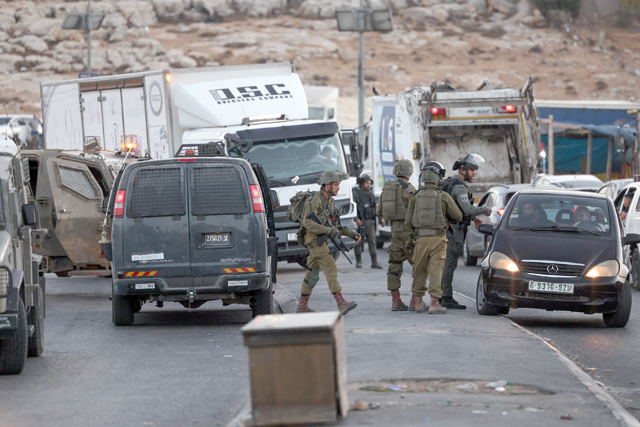 Israeli forces talk to passengers in traffic after closing an entrance of the Palestinian town of Anata as they conduct a manhunt following a shooting attack in the Palestinian Shuafat refugee camp in Israeli-occupied East Jerusalem, on Sunday (AFP photo)