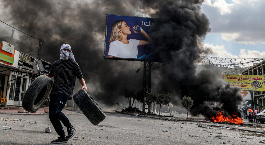 A masked man walks with tyres past other burning tyres during confrontations in the village of Deir Sharaf near the western entrance of the city of Nablus in the occupied West Bank on Thursday (AFP photo)