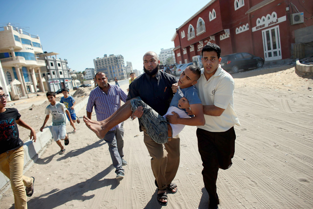 In this file photo taken on July 16, 2014, Palestinian employees of Gaza City’s Al Deira hotel carry a wounded boy following an Israeli strike nearby on the beach (AFP photo)