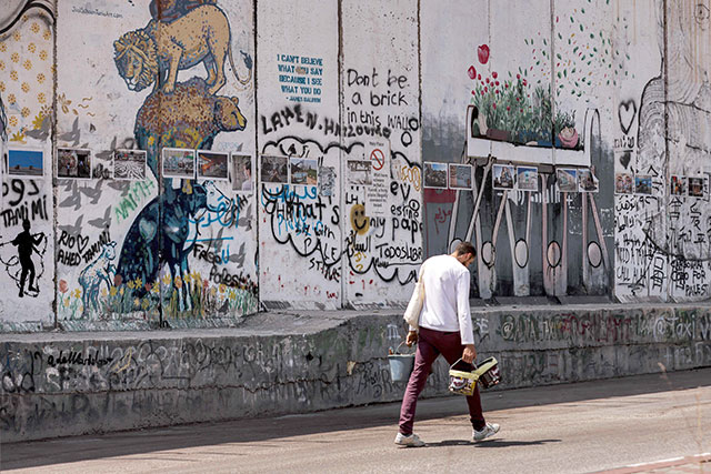 Palestinian artist Taqi Spateen walks carrying buckets of paint after finishing his latest mural on the theme of violence against journalists covering the Israeli-Palestinian conflict on a section of Israel's controversial separation barrier in Bethlehem on Wednesday (AFP photo)