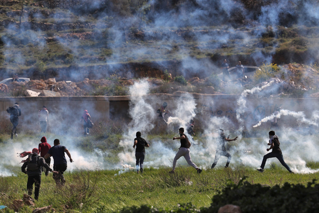 Palestinians run for cover during confrontations with Israeli forces at the northern entrance of Ramallah, near the Israeli settlement of Beit Eil, in the occupied West Bank, on Monday (AFP photo)