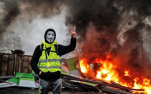 A protester wearing a Guy Fawkes mask makes the victory sign near a burning barricade during a protest of yellow vests against rising oil prices and living costs in Paris on Saturday (AFP photo)