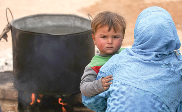 A displaced Syrian child, who fled the countryside surrounding the Deash group stronghold of Raqqa, looks on as he is being held by a woman at a temporary camp in the village of Ain Issa on Friday (AFP photo)