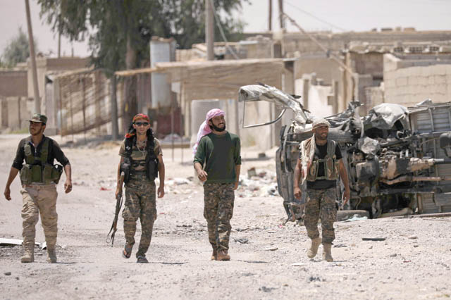 Syrian Democratic Forces fighters walk past a damaged vehicle in Raqqa’s western neighbourhood of Jazra, Syria, Sunday (Reuters photo)