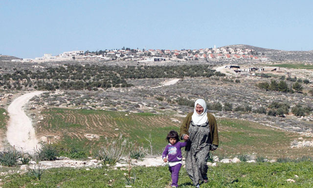 A picture taken on Monday shows a Palestinian woman and a child walking in the Bani Naaim village with the Israeli settlement of Bani Hever, southwest of the Israeli occupied West Bank city of Hebron, seen in the background (AFP photo)