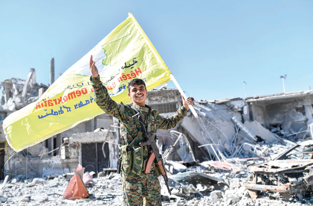 A member of the Syrian Democratic Forces, backed by US special forces, holds up their flag at the iconic Al Naim square in Raqqa on Tuesday (AFP photo)