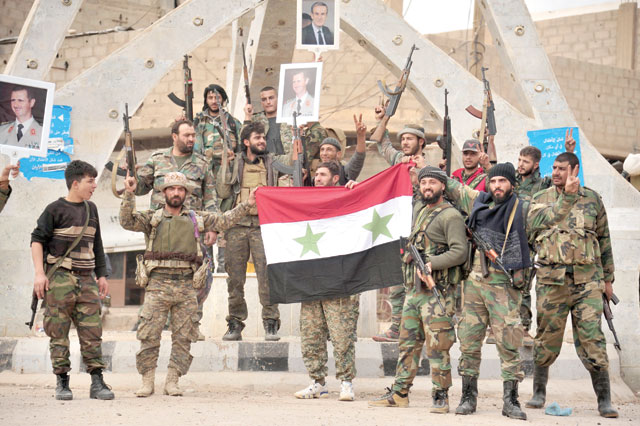 This handout photo released by the official Syrian Arab News Agency on Tuesday shows members of the pro-Syrian government forces posing with portraits of Syrian President Bashar Assad while waving a national flag as they gather in a public square in the Syrian border town of Albu Kamal (AFP photo)
