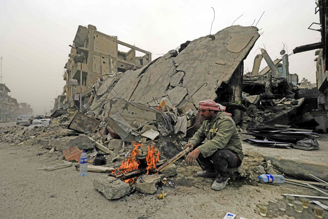 A Syrian man sits by a fire on a destroyed street in Raqqa on Wednesday, two months after YPG-led Syrian Democratic Forces captured the city from the Daesh group (AFP photo)