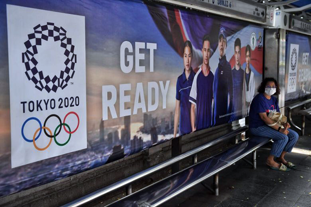  A woman wears a facemask as she sits at a bus stop advertising the Tokyo 2020 Summer Olympics in Bangkok, in undated photo (AFP photo)