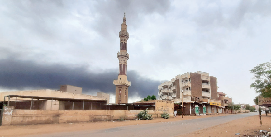 Smoke rises above buildings behind a nearly deserted street in Khartoum on Saturday (AFP photo)
