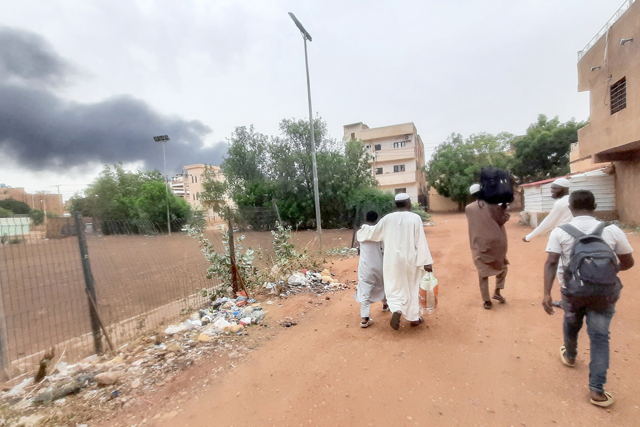 Smoke rises above buildings as people flee with some belongings, in Khartoum, on Saturday (AFP photo)