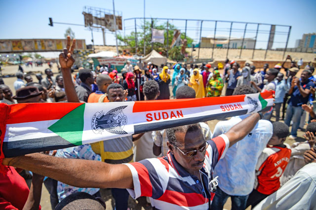 A Sudanese man waves a banner showing the national flag colours as protesters gather and chant slogans at the protest outside the army headquarters in the capital Khartoum on Tuesday (Reuters  photo)