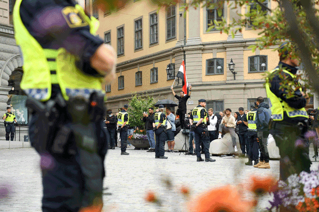 Policemen stand next to demonstrators, among them a protester (background, centre) holding the flag of Iraq, at Mynttorget square in Stockholm, Sweden, on Monday (AFP photo)