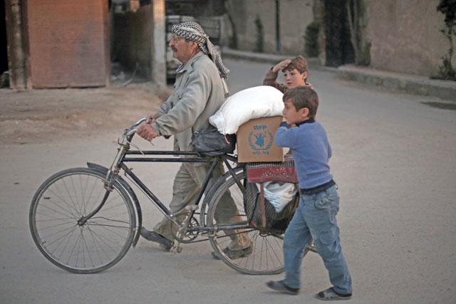 A Syrian man and his children carry sacks of wheat and aid, provided by the World Food Programme, in Kafr Batna, in the rebel-held Eastern Ghouta area, on the outskirts of the capital Damascus, on Tuesday (AFP photo)