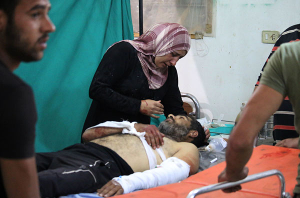 A Syrian woman stands over a wounded man at a field hospital in the southern Syrian city of Daraa after he was wounded in a strike by a government forces’ missile on the rebel-held part of the city on  Monday (AFP photo)