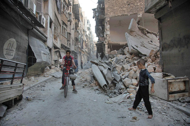 Syrians walk through the rubble following an air strike on the regime-controlled neighbourdhood of Karm Al Jabal on Sunday (AFP photo)