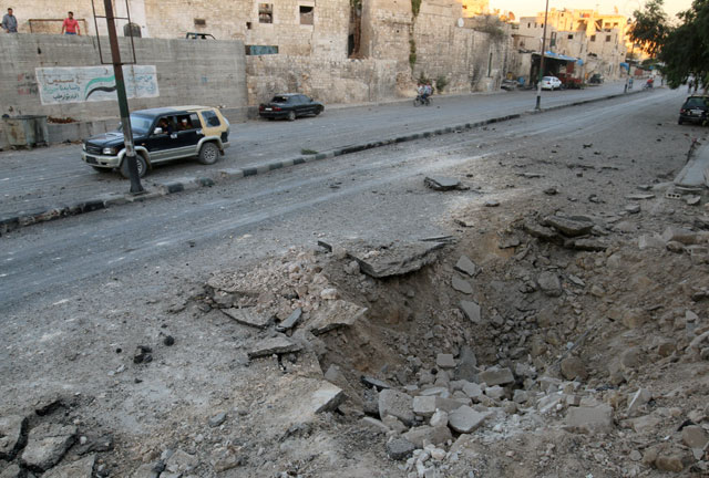 People ride a vehicle past a crater in the rebel-held Qadi Askar neighbourhood of Aleppo, Syria, on Monday (Reuters photo)