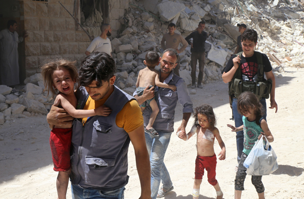 Syrian men carry injured children amid the rubble of destroyed buildings following reported air strikes on the rebel-held neighbourhood of Al Mashhad in the northern city of Aleppo, on Monday (AFP photo)