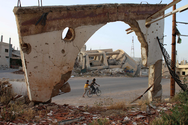 Photo taken through an arch remaining from a destroyed building shows Syrian boys on a bicycle on Saturday in the southern Syrian city of Daraa (AFP photo)